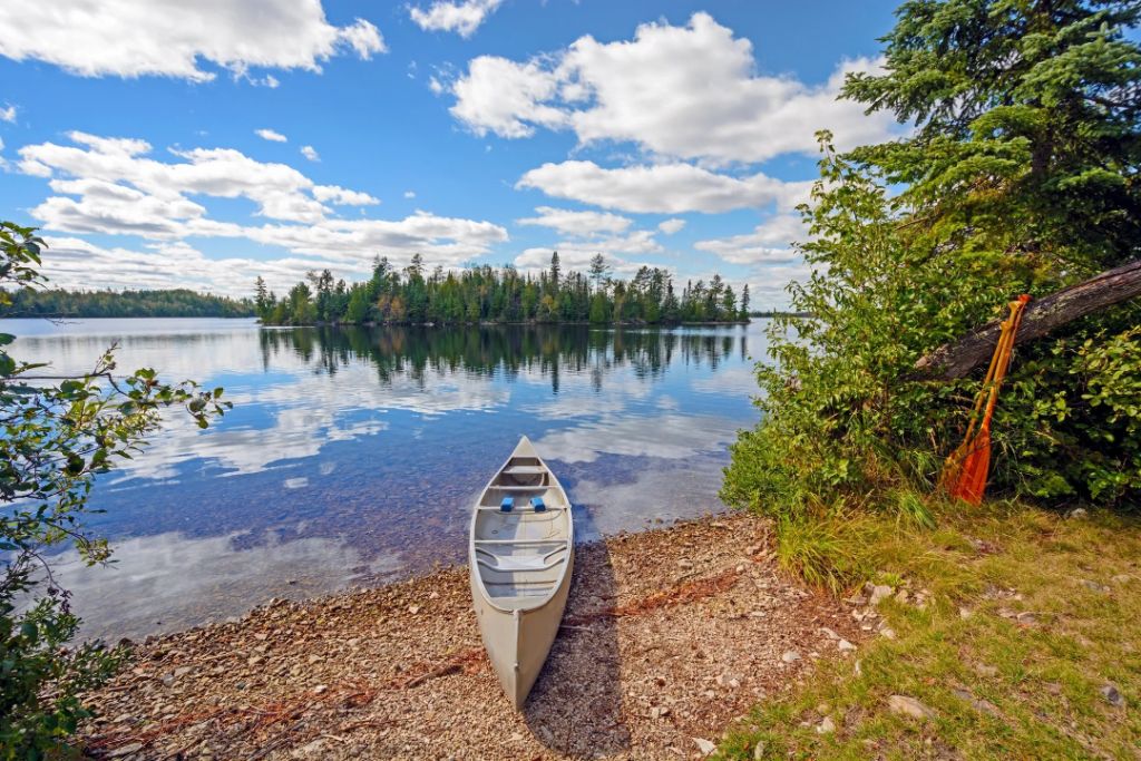 A canoe resting on the rocky shore of a calm Maine lake surrounded by pine trees on a sunny day